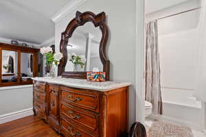 Bathroom with shower / tub combo, vanity, ornamental molding, and dark wood-type flooring