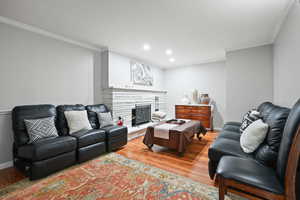 Living room with ornamental molding, wood finished floors, recessed lighting, and a stone fireplace
