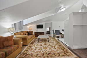 Living area with a textured ceiling, carpet floors, vaulted ceiling, and a desk