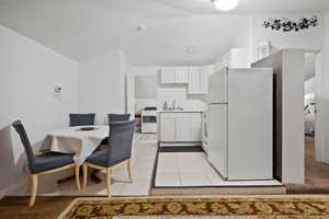 Kitchen featuring white appliances, white cabinets, light countertops, light tile patterned floors, and lofted ceiling