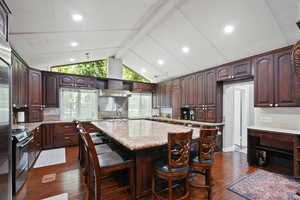Kitchen with dark brown cabinetry, a kitchen island with sink, dark wood-type flooring, a kitchen bar, and recessed lighting
