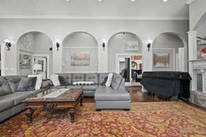 Living room with arched walkways, dark wood-type flooring, crown molding, and a high end fireplace