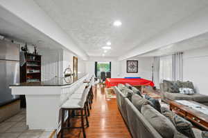 Living room with a textured ceiling, light wood-style floors, billiards, bar area, and recessed lighting