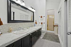 Bathroom featuring a closet, double vanity, a stall shower, tasteful backsplash, and lofted ceiling