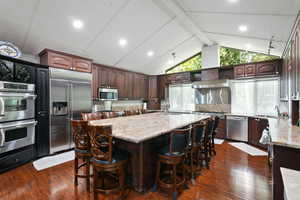 Kitchen featuring dark brown cabinetry, a kitchen breakfast bar, dark wood finished floors, stainless steel appliances, and recessed lighting