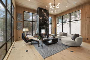 Living room with wooden walls, a multi sided fireplace, light wood finished floors, wooden ceiling, and suspended lighting