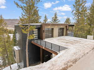Snow covered structure featuring a garage and driveway