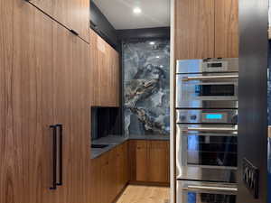 Kitchen with modern cabinets, brown cabinets, double oven, light wood-type flooring, and recessed lighting