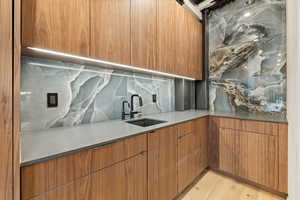 Kitchen with modern cabinets, decorative backsplash, light wood-type flooring, wood finish cabinets, and light stone countertops
