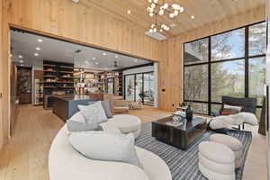 Living room with light wood-style floors, wooden walls, hanging lights, a high wooden ceiling, and wine cooler