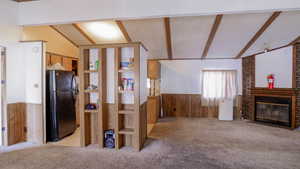 Unfurnished living room featuring wood walls, wainscoting, light colored carpet, and a fireplace