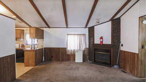 Unfurnished living room with wooden walls, a wainscoted wall, light carpet, a fireplace, and beam ceiling