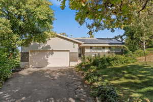View of front of home featuring brick siding, driveway, roof mounted solar panels, a garage, and a front lawn