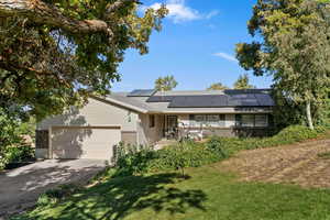 View of front of property featuring driveway, roof mounted solar panels, brick siding, a front lawn, and a garage