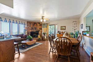 Dining area with a stone fireplace, wood finished floors, a textured ceiling, and ceiling fan