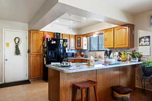 Kitchen with brown cabinetry, black fridge, a kitchen bar, a peninsula, and a textured ceiling