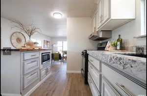 Kitchen featuring black electric range oven, light wood-style flooring, under cabinet range hood, and white cabinets
