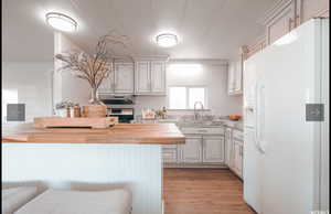 Kitchen featuring white refrigerator with ice dispenser, wooden counters, a textured ceiling, light wood finished floors, and stainless steel stove