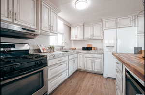 Kitchen with stainless steel range with gas stovetop, white fridge with ice dispenser, under cabinet range hood, wooden counters, and light wood-style flooring