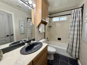 Bathroom with a textured ceiling, shower / bath combination with curtain, vanity, and dark tile patterned floors