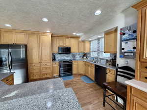 Kitchen with stainless steel appliances, light stone counters, light wood-style flooring, recessed lighting, and a textured ceiling
