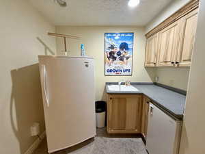 Bar area featuring freestanding refrigerator, a textured ceiling, and light brown cabinets