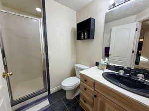 Full bath featuring dark tile patterned flooring, a stall shower, vanity, and a textured ceiling
