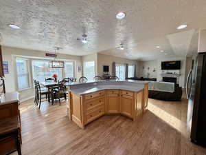 Kitchen with freestanding refrigerator, a textured ceiling, light wood finished floors, decorative light fixtures, and light stone countertops