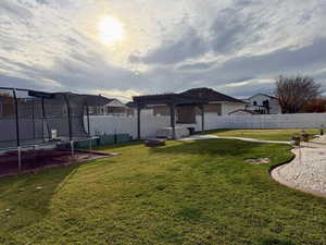 Fenced backyard featuring a trampoline, a pergola, and a patio area
