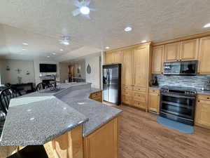 Kitchen with appliances with stainless steel finishes, light stone counters, a textured ceiling, light wood-style floors, and tasteful backsplash