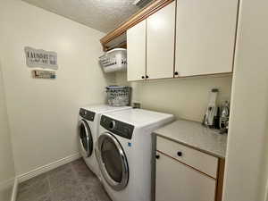Laundry area with cabinet space, a textured ceiling, washer and dryer, and dark tile patterned flooring