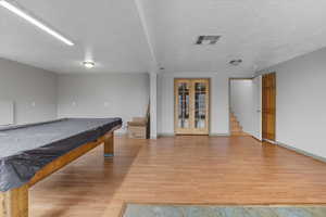 Recreation room featuring french doors, light wood finished floors, pool table, and a textured ceiling