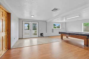 Rec room with french doors, a textured ceiling, light wood finished floors, beamed ceiling, and billiards table