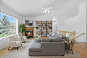 Living room featuring light wood-type flooring, a glass covered fireplace, vaulted ceiling, and a ceiling fan