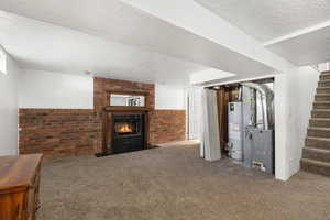 Finished basement with carpet, a textured ceiling, gas water heater, stairs, and a large fireplace