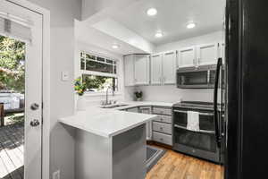 Kitchen featuring black appliances, light wood-style floors, recessed lighting, a peninsula, and light stone countertops