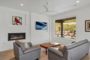 Living room featuring light wood-type flooring, recessed lighting, a glass covered fireplace, and a ceiling fan