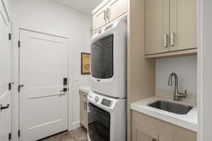Laundry area featuring stacked washer and clothes dryer, cabinet space, and dark tile patterned flooring
