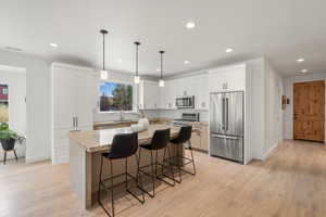 Kitchen featuring stainless steel appliances, a kitchen breakfast bar, pendant lighting, white cabinets, and a kitchen island