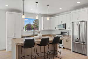 Custom kitchen featuring stainless steel appliances, light wood flooring, pendant lighting, an oversized granite island.