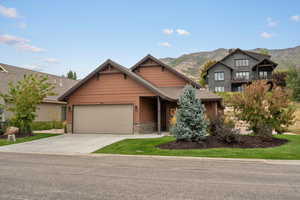 Craftsman house with stone siding, concrete driveway, a mountain view, and an attached garage