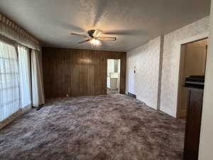 Unfurnished living room with a textured ceiling, dark carpet, and ceiling fan
