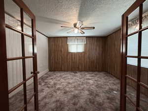 Unfurnished room featuring a textured ceiling, dark colored carpet, wood walls, a ceiling fan, and crown molding