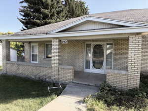 Entrance to property with brick siding, covered porch, a yard, and roof with shingles