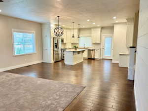 Kitchen featuring a center island, a chandelier, dark wood-type flooring, a textured ceiling, and appliances with stainless steel finishes