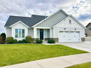 Craftsman house featuring stone siding, board and batten siding, a front yard, and driveway