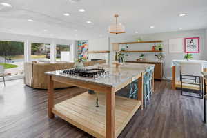 Kitchen with decorative light fixtures, light stone counters, dark wood-style floors, open shelves, and recessed lighting