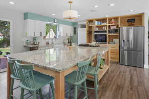 Kitchen with stainless steel appliances, decorative light fixtures, recessed lighting, light stone counters, and dark wood-type flooring