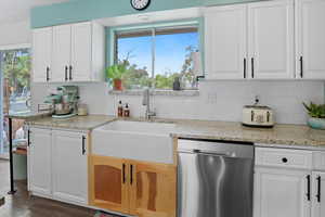 Kitchen with stainless steel dishwasher, white cabinetry, light stone counters, and healthy amount of natural light
