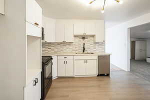Kitchen featuring decorative backsplash, white cabinets, black range with electric cooktop, and light wood-style floors